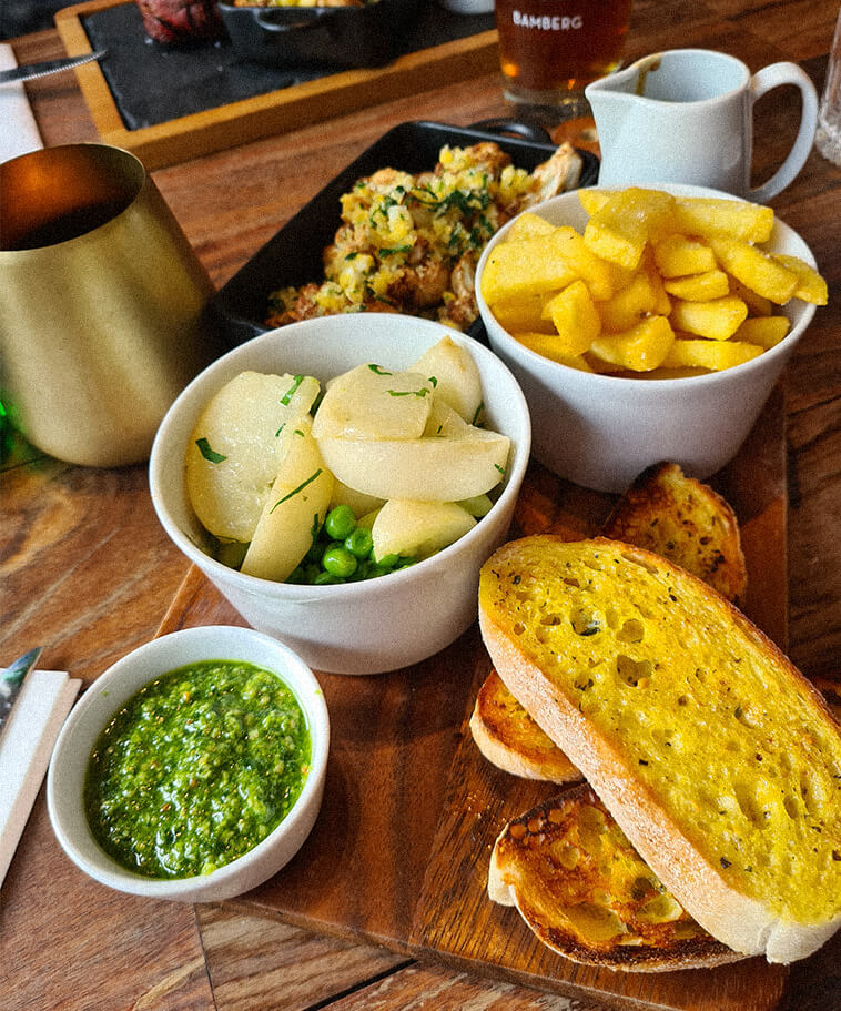 Ein reich gedeckter Essenstisch mit gekochten Kartoffeln, Gemüse, leicht geröstetem Brot und einer grünen Soße