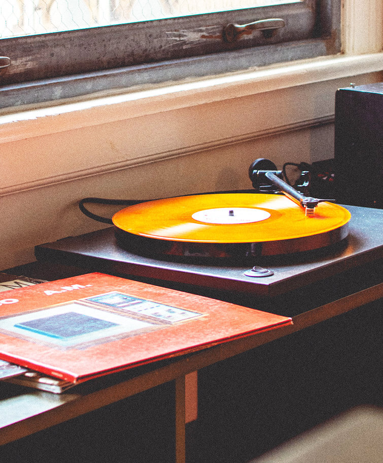 Ein alter Plattenspieler mit einer orangen Schallplatte. Nebendran ein kleiner, bunter Stapel Schallplatten